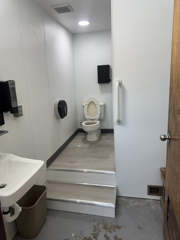 Renovated restroom with white wall panels, a raised floor with steps and a grab bar