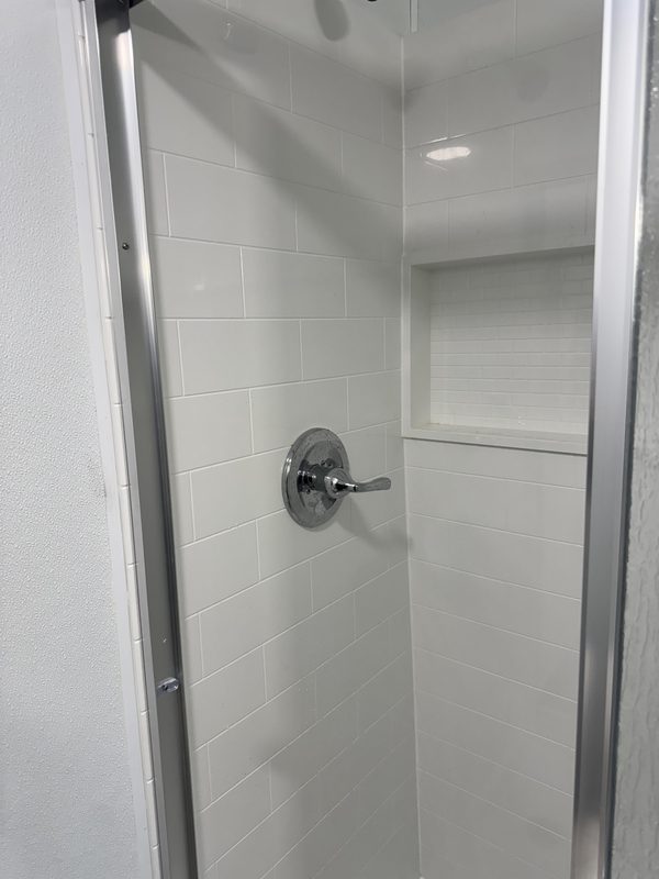 White subway-tile shower with a chrome valve and a recessed niche
