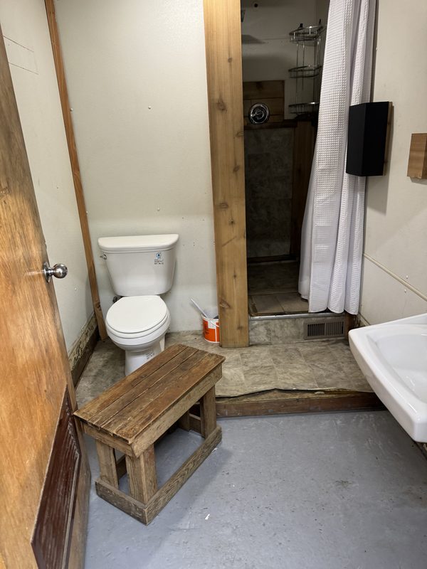 Restroom before renovation, with worn flooring and a shower curtain